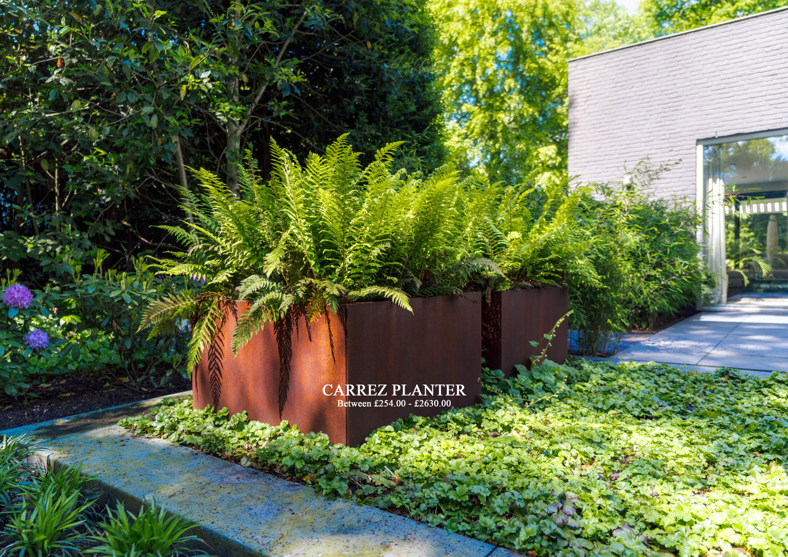 Rust-colored metal planter filled with lush ferns in a garden beside a modern brick building.